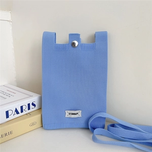 Detail of light blue knit phone bag featuring a metal snap closure and brand label