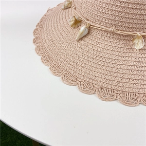 Detail of wavy brim straw hat with woven texture and decorative natural sea shells