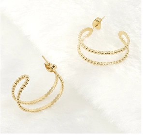 Detail of 18K gold double-layer earrings with bead texture on a white plush surface