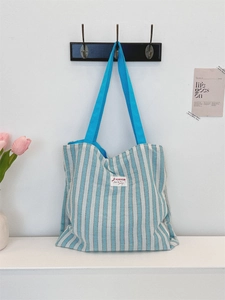 Dettaglio della borsa tote in tela a righe con tracolle blu e toppa con logo bianco