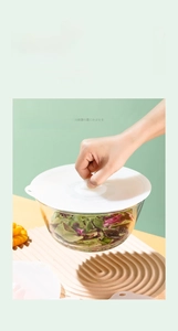 Detail of white silicone suction lid sealing a glass bowl with fresh salad inside