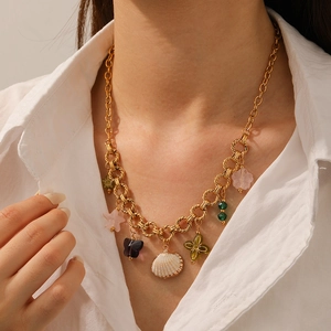 Collier à grosse chaîne en acier doré avec coquillage et breloques colorées sur modèle