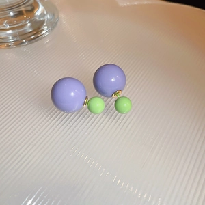 Macro view of double bead earrings featuring a large purple sphere and a small green bead