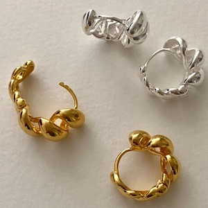 Detail of minimalist twisted hoop earrings in gold and silver finish on soft background