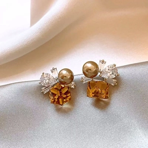 Close-up of luxury geometric stud earrings with amber crystal and pearls on silk