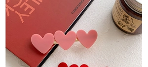 Detailed view of pink acrylic heart hair clips with golden metal base on a warm desk