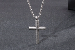 Detailed close-up of a vintage silver cross pendant on a textured dark fabric background