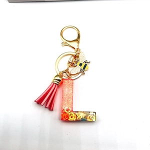 Macro view of transparent resin letter L keychain with red sequins and bee charm