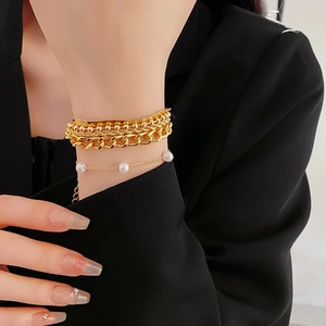 Detail of layered gold-plated bracelets featuring snake chain and pearl accents