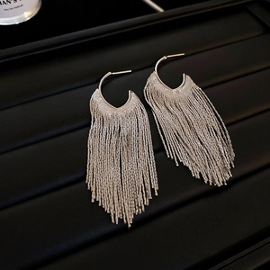 Detail of silver long tassel earrings with C-shaped hooks on black textured leather