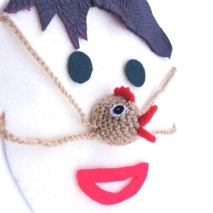 Handmade knitted chicken nose warmer with purple hair and green felt eyes on white background