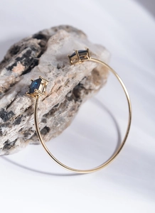 Close-up of golden adjustable bangle with blue square gemstones on a natural stone base