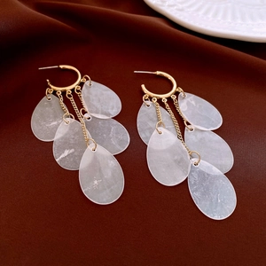 Detail of drop-shaped white shell pendants hanging on gold bamboo textured hoop earrings