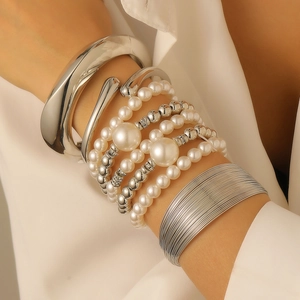 Detail of layered jewelry set featuring silver bracelets and multiple sizes of white pearls