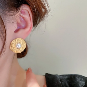 Close-up of vintage golden spiral earrings with faux pearls worn by a female model