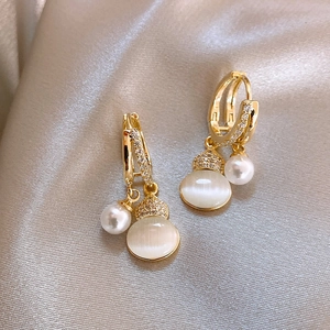 Macro view of gold hoop earrings featuring opal charms, pearls, and zircon stones on silk