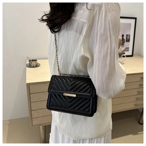 Detail of a black quilted crossbody bag with gold chain strap and elegant V-pattern stitching