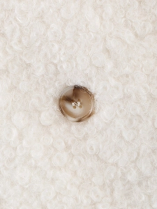 Close-up of white curly bouclé faux fur fabric and tortoiseshell button detail
