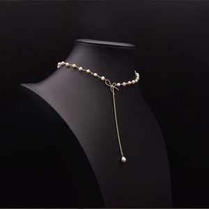Macro detail of natural pearls with gold chain and elegant bow pendant on a black bust