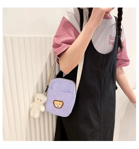 Detail view of purple corduroy crossbody bag with brown bear patch and plush charm