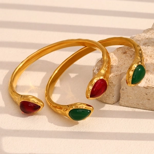 Detail of 18K gold snake head bangle with red and green gemstones on hammered metal