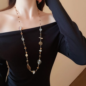 Dettaglio della collana lunga con perline champagne e marroni su una modella