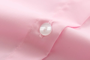Macro shot of pink cotton fabric texture with a white button on a women's shirt