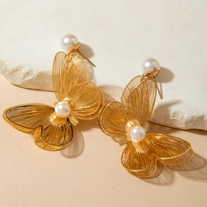 Close-up of golden alloy butterfly earrings with pearls on white stone background
