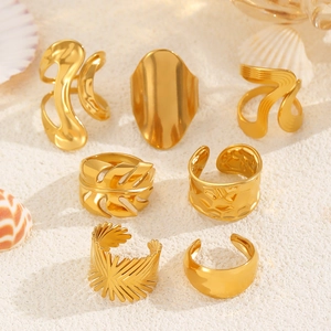 Set of 7 gold irregular stainless steel rings arranged on warm sand texture background