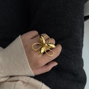 Detailed view of oversized golden flower petal ring worn on hand with metallic texture