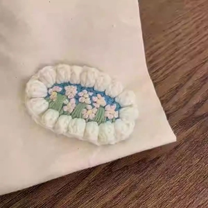 Detail einer handgefertigten ovalen Haarspange mit Stickerei: rosa Blume auf blau