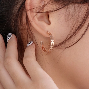 Macro shot of rose gold chain-link C-shaped earrings worn by a model in detail