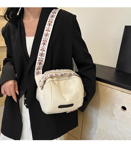 Detailed view of cream nylon crossbody bag featuring an embroidered ethnic style wide strap