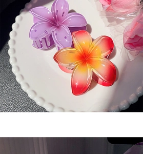Detail of violet and orange plumeria hair claws on a white plate with floral accents