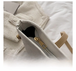 Detail of golden metal zipper and embossed texture on white leather tote bag