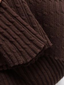 Makroaufnahme eines dunkelbraunen Strickpullovers mit Zopfmustern und gerippten Bündchen