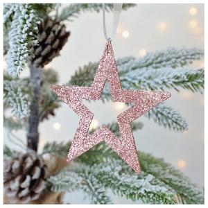 Macro shot of pink glitter star ornament with cutout design hanging on a Christmas tree