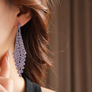 Gros plan détaillé de longues boucles d'oreilles à pompons violets avec strass sur un mannequin