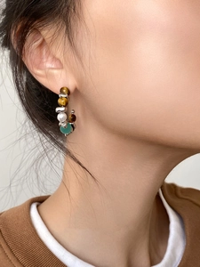 Detail of C-shaped hoop earrings featuring tiger eye stones, pearls and silver beads on a model