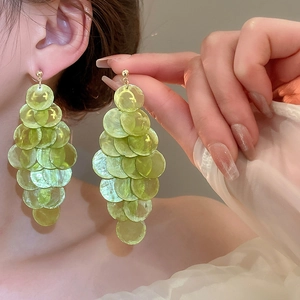 Close-up of light green shell-style layered round tassel earrings worn by a model