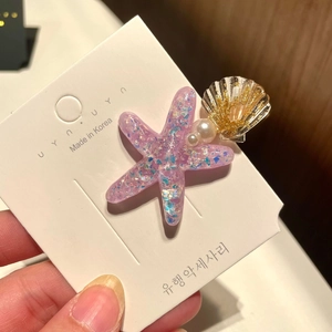 Detail of glitter starfish and shell hair clip with pearls on a display card