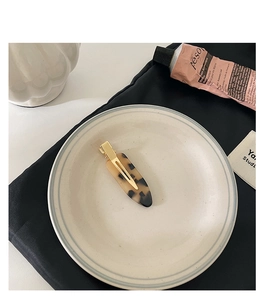 Detail of tortoise shell acetate hair clip with golden metal base on a white ceramic plate