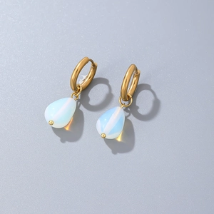 Macro detail of gold hoop earrings with white teardrop opal pendants on grey surface
