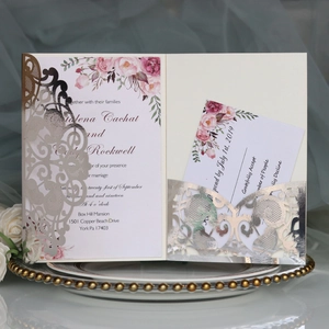 Detail of silver laser-cut wedding invitation with floral insert on a gold beaded tray