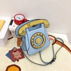 Close-up of creative retro telephone-shaped crossbody bag with gold dial and strap