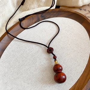 Detail of wooden gourd pendant with gold metal accents on brown cord necklace
