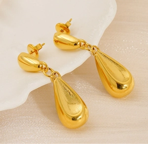 Close-up of gold hollow teardrop earrings with a polished finish on a white shell plate