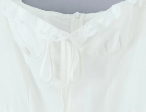Detail of white mini dress neckline featuring delicate lace trim and front tie closure