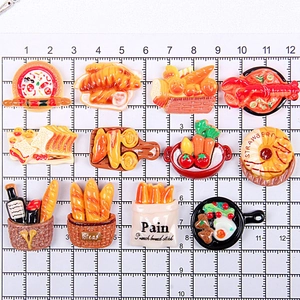 Flat lay of 12 mini resin food models including croissants and pizza on a cutting mat