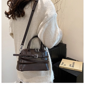 Detail of dark brown shell bag in glossy finish paired with a cream knit sweater